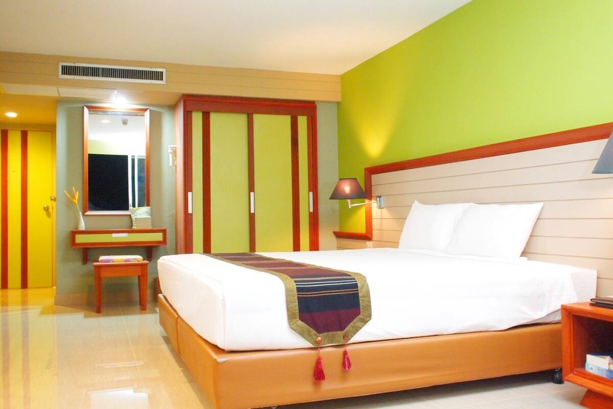 A hotel room with a bed, bedside table, lamp, and a mirror.
