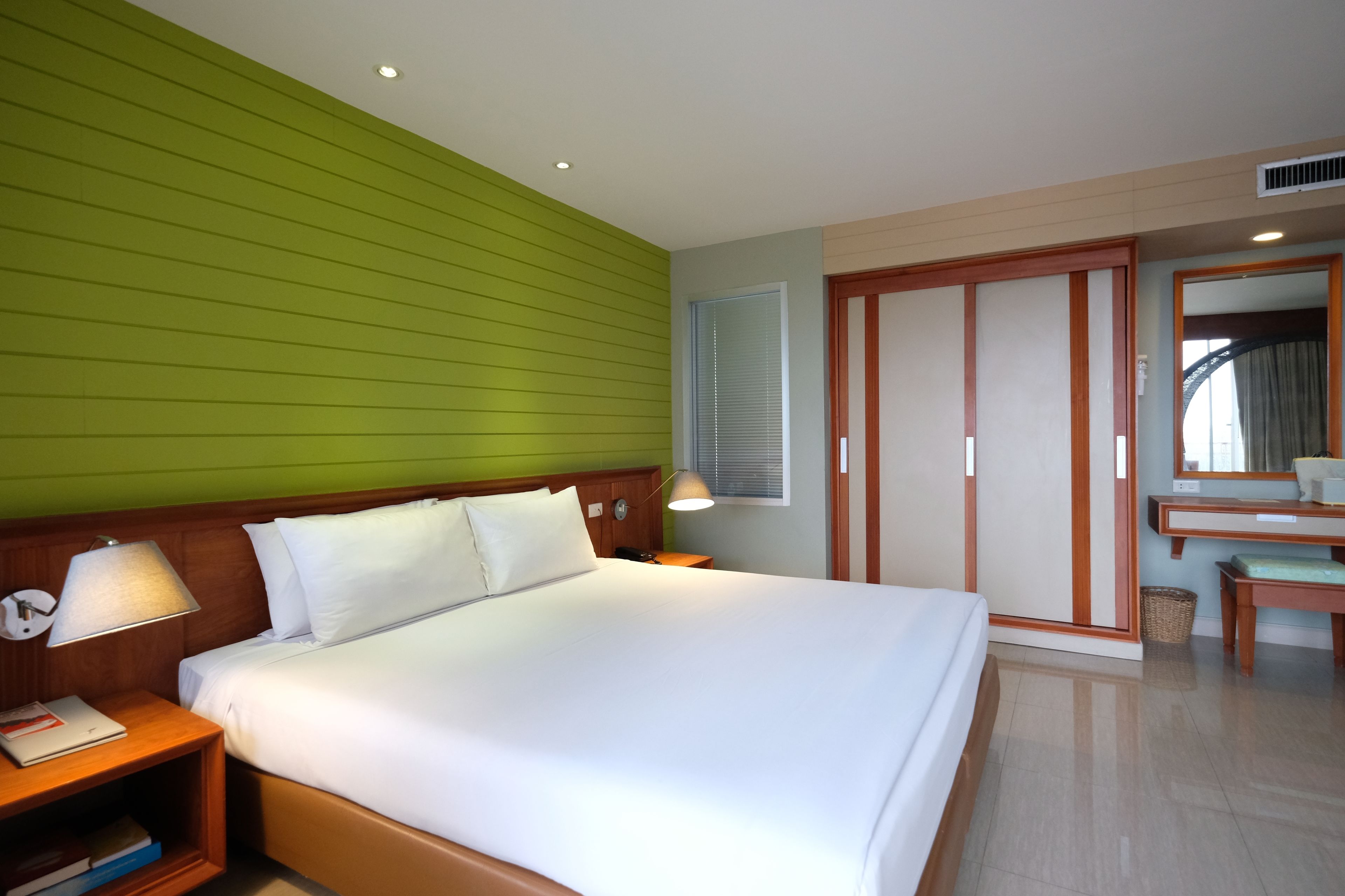 A hotel room with a large bed, wooden headboard, bedside tables, a mirror, and a wardrobe.