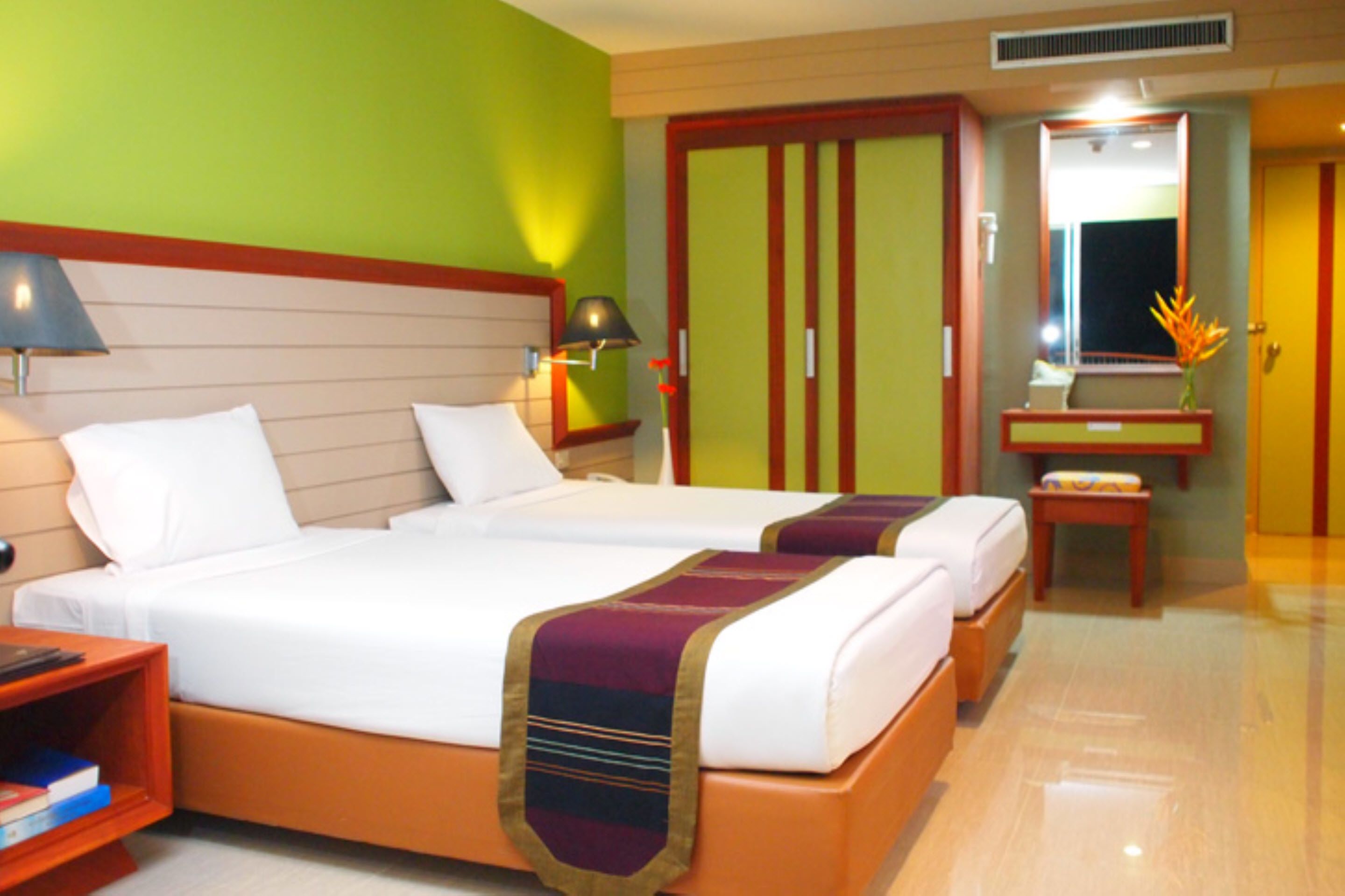 Een hotelkamer met twee bedden, een nachtkastje, een bureau, een spiegel en een kledingkast.