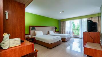Habitación de hotel con dos camas, un escritorio, un televisor y un balcón con vista a zonas verdes.