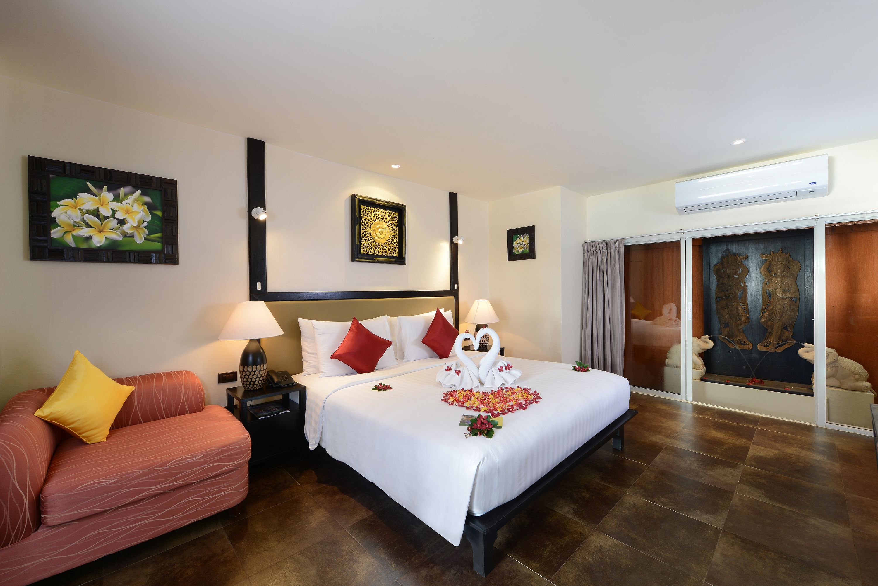 Une chambre d’hôtel comprenant un lit, un canapé, une table de chevet et un climatiseur fixé au mur.