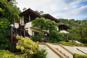A multi-story building with a balcony, surrounded by lush greenery and palm trees.