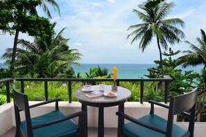 Enjoy a romantic breakfast for two on this serene balcony overlooking the ocean, surrounded by lush greenery and palm trees.