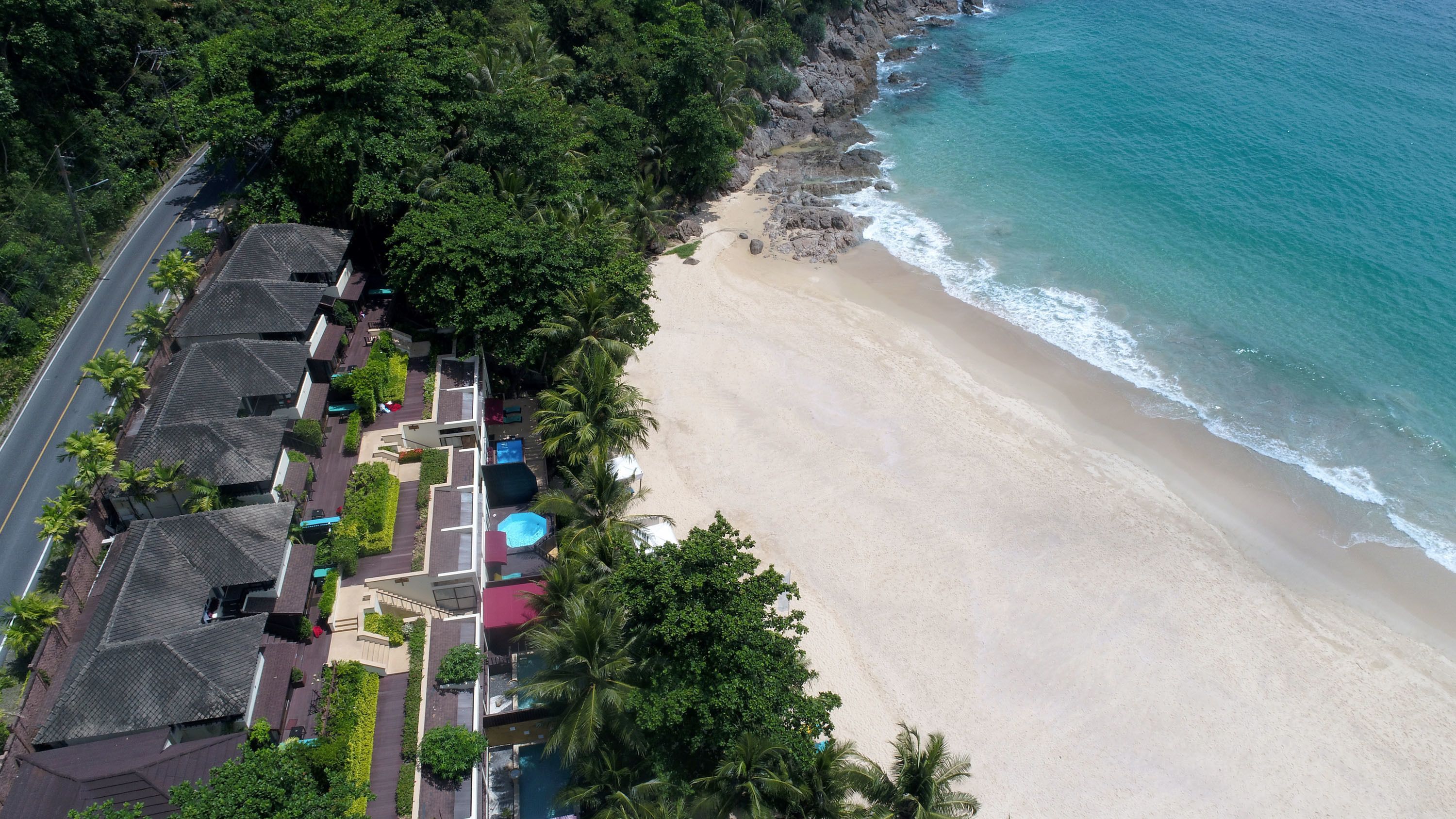 An aerial view of a beachfront property with a road, houses, and a beach.