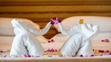 Two white towels shaped like elephants on a bed with scattered flower petals.