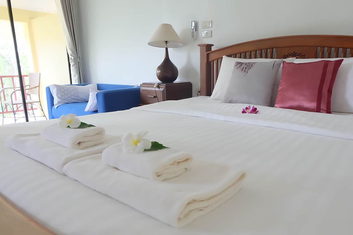 Cama bem arrumada com lençóis brancos, cabeceira de madeira e mesa de cabeceira com abajur.