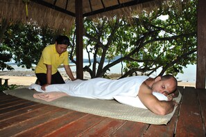 A man receiving a massage on a wooden deck with a beach view in the background.