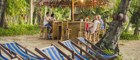 A beachside bar with bamboo furniture and striped beach chairs.