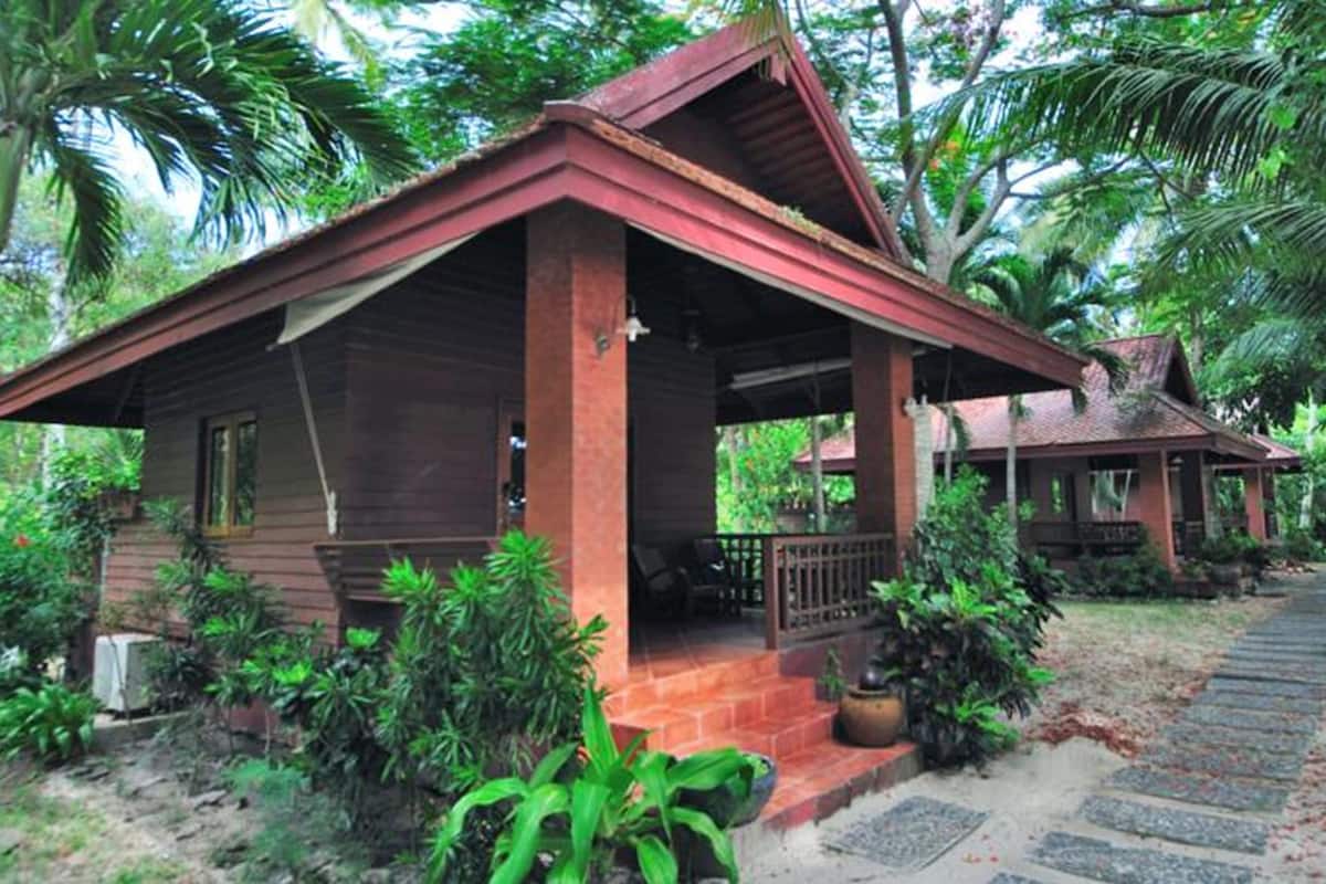 Uma casa de madeira com varanda, cercada por vegetação exuberante e palmeiras.