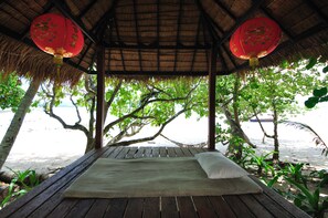 A wooden deck with a thatched roof, a bed with a pillow, and red lanterns.