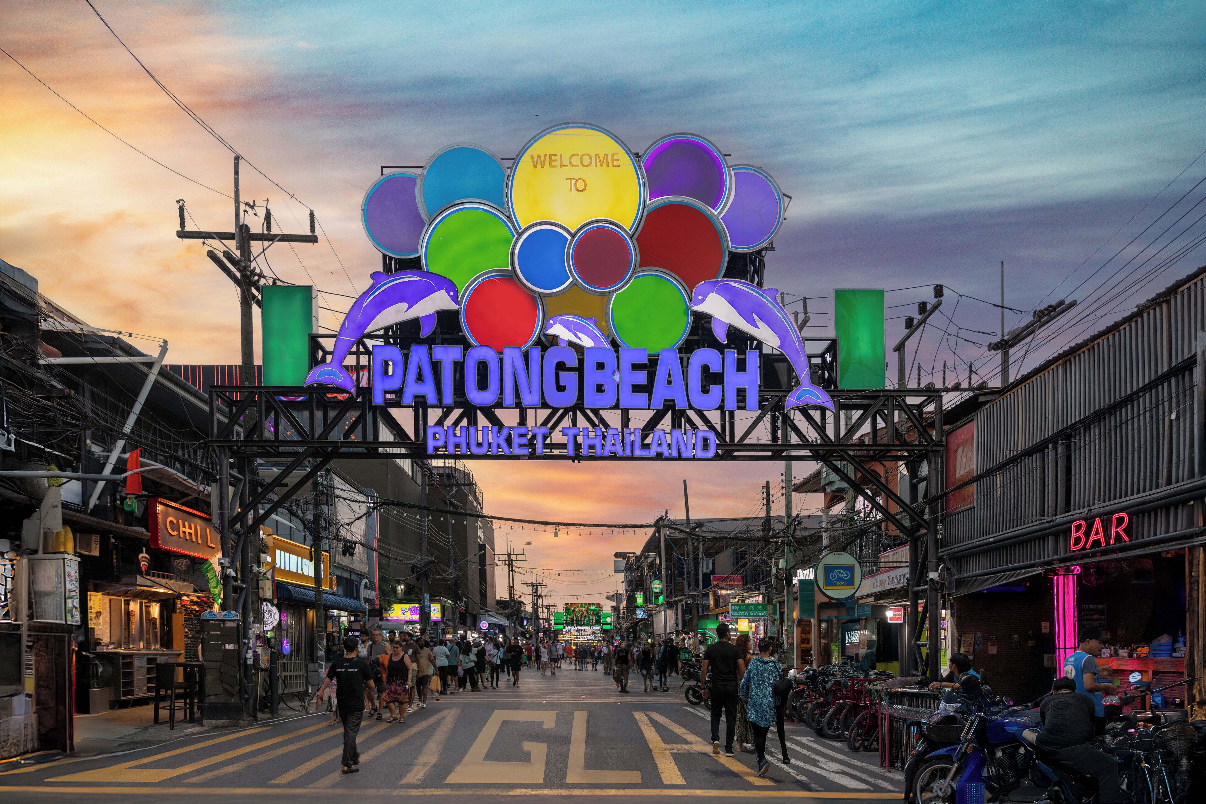 Une rue animée avec une grande enseigne indiquant : « Bienvenue à Patong Beach, Phuket, Thaïlande ».
