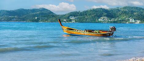 A boat on a calm sea with a beach and hills in the background.