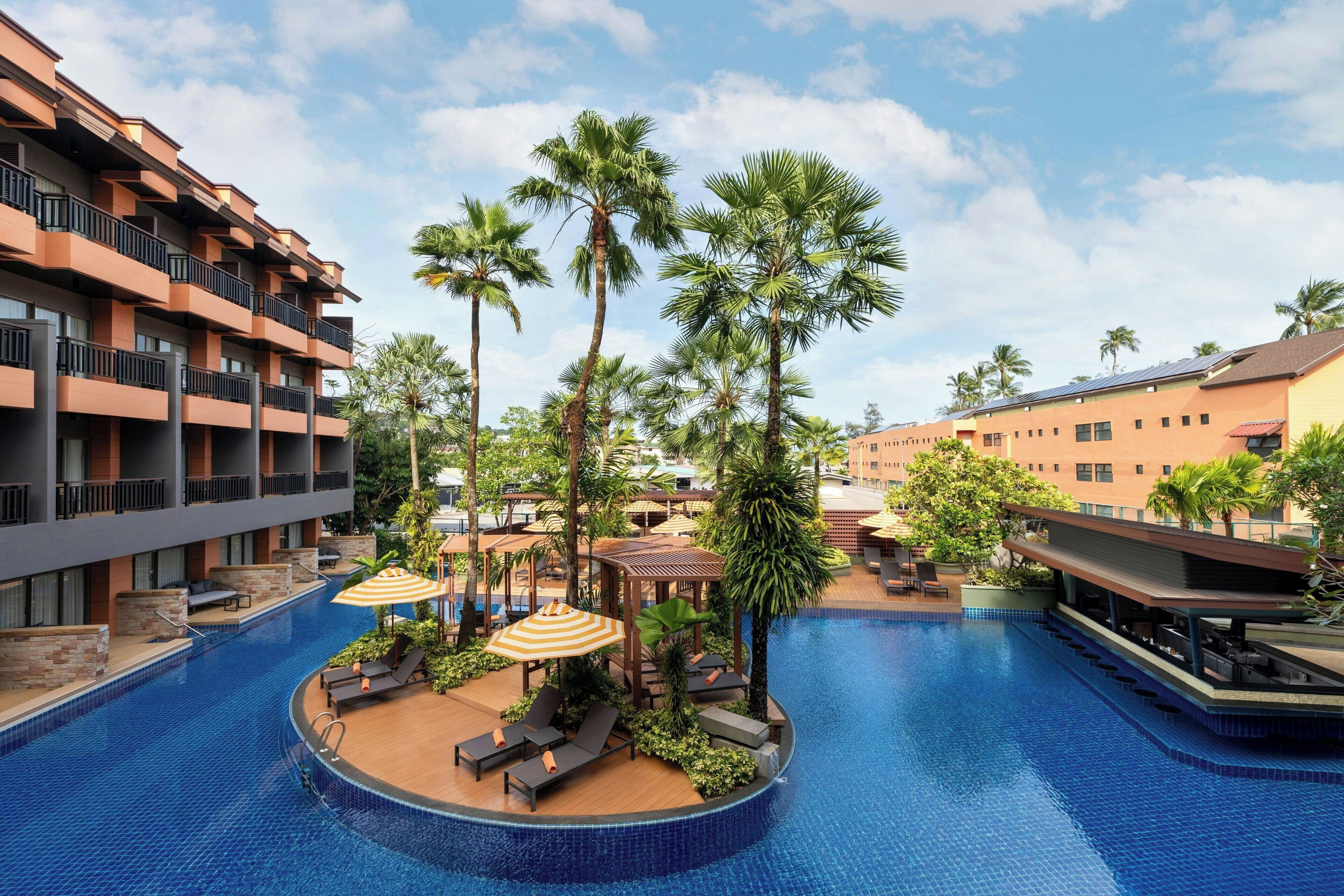 A hotel pool area with multiple levels of balconies, palm trees, and sun loungers.
