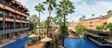 A hotel pool area with multiple levels of balconies, palm trees, and sun loungers.