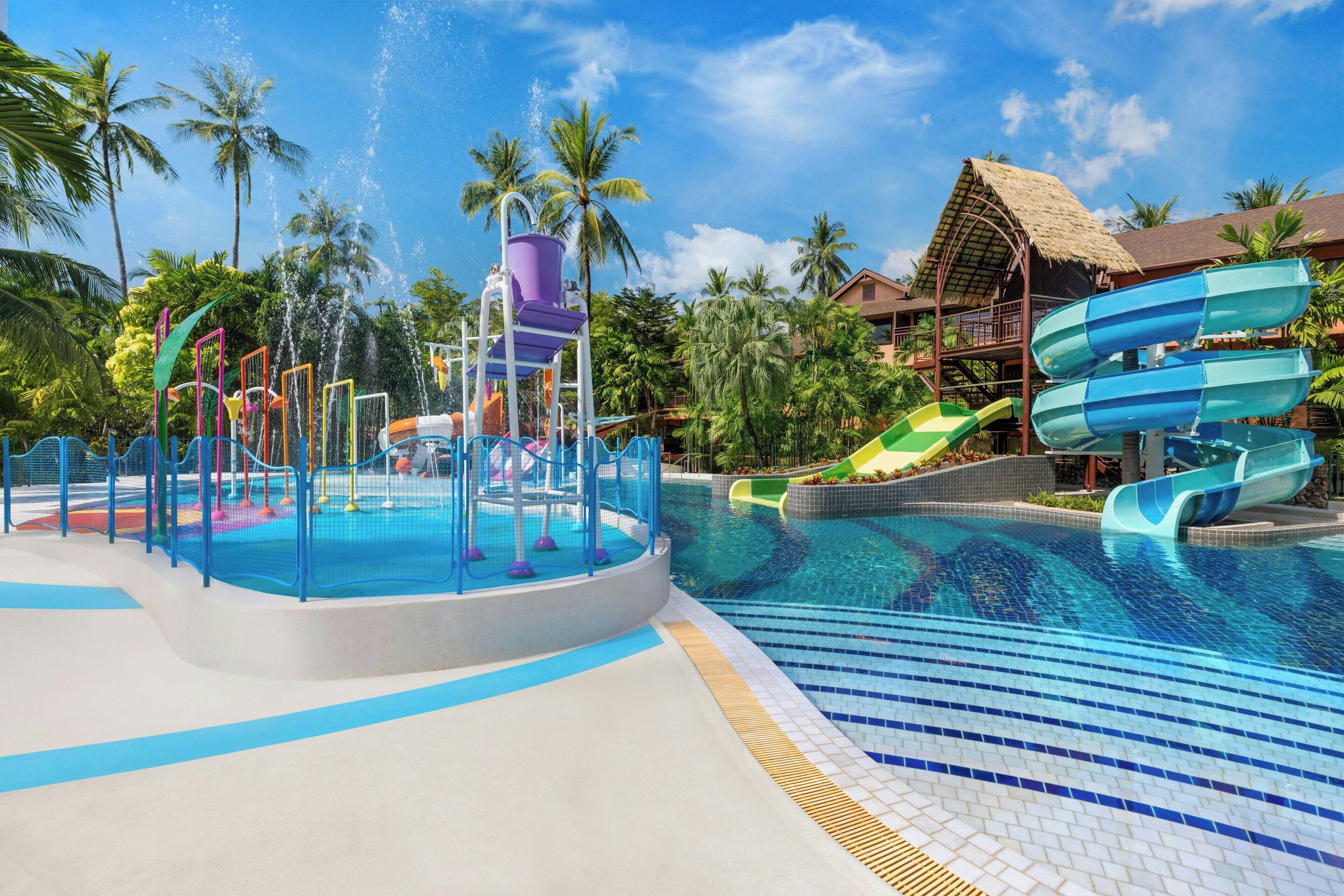 A water park with a pool, slides, and a thatched-roof building.