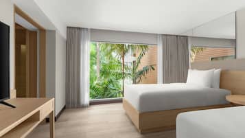 A modern hotel room with a large bed, a desk, and a view of greenery through the window.