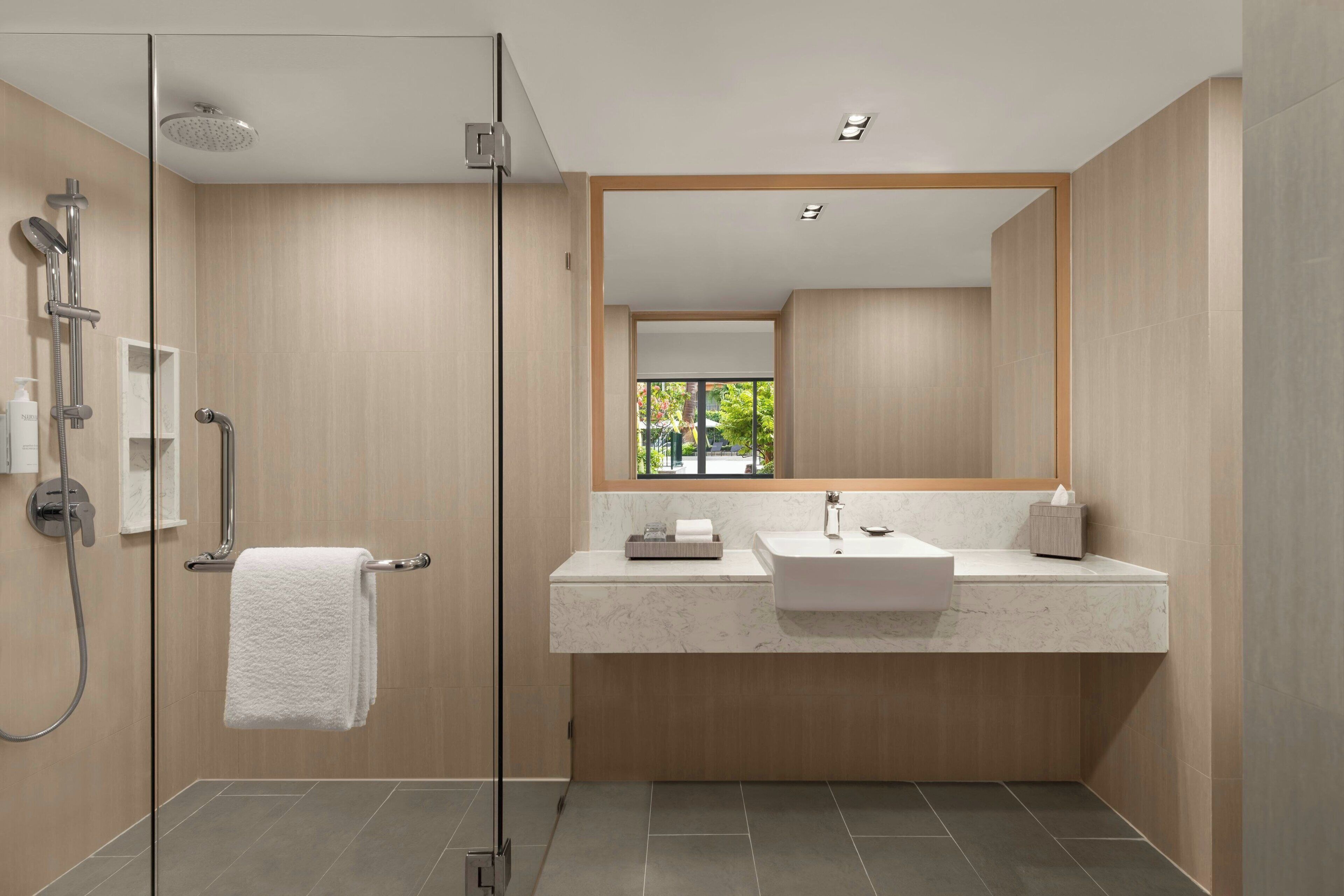 A modern bathroom with a glass shower enclosure, a white sink, and a large mirror.