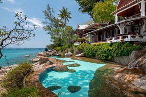 A resort with a pool surrounded by rocks and trees, overlooking the ocean.