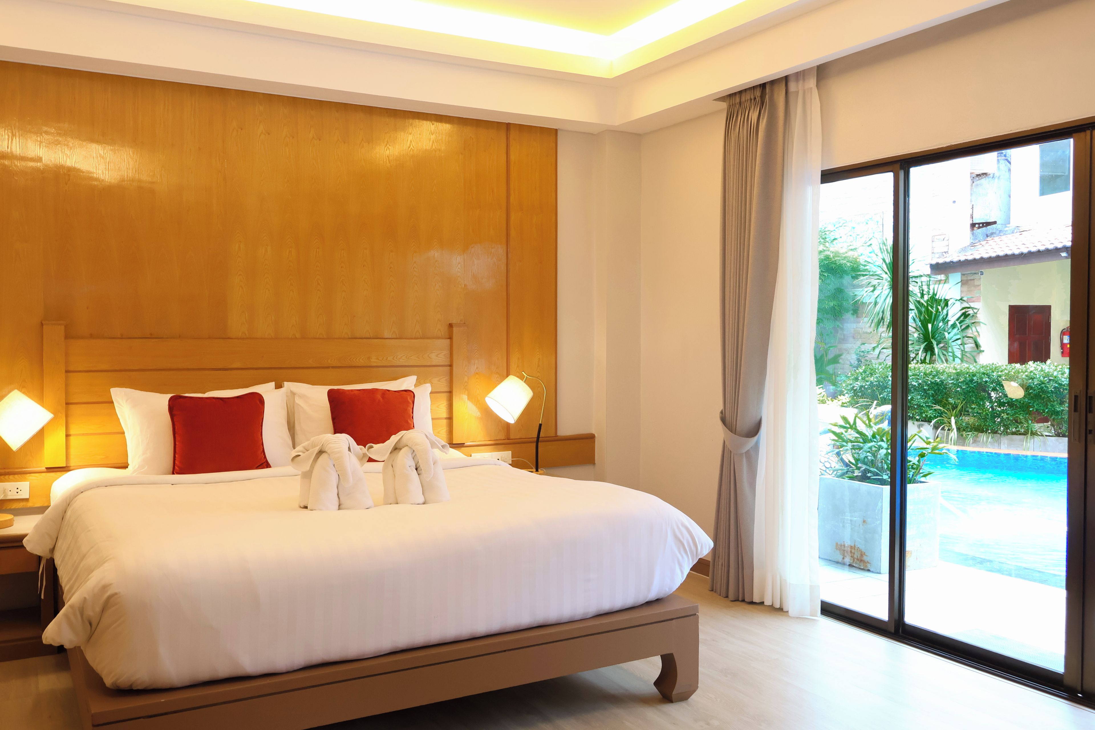 A hotel room with a large bed, two bedside lamps, a view of a swimming pool, and a sliding glass door.