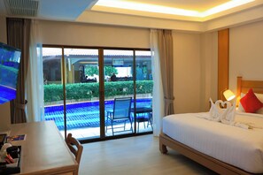 A hotel room with a bed, a desk, a TV, and a view of an outdoor pool area. - Baan Boa Resort  (Patong)