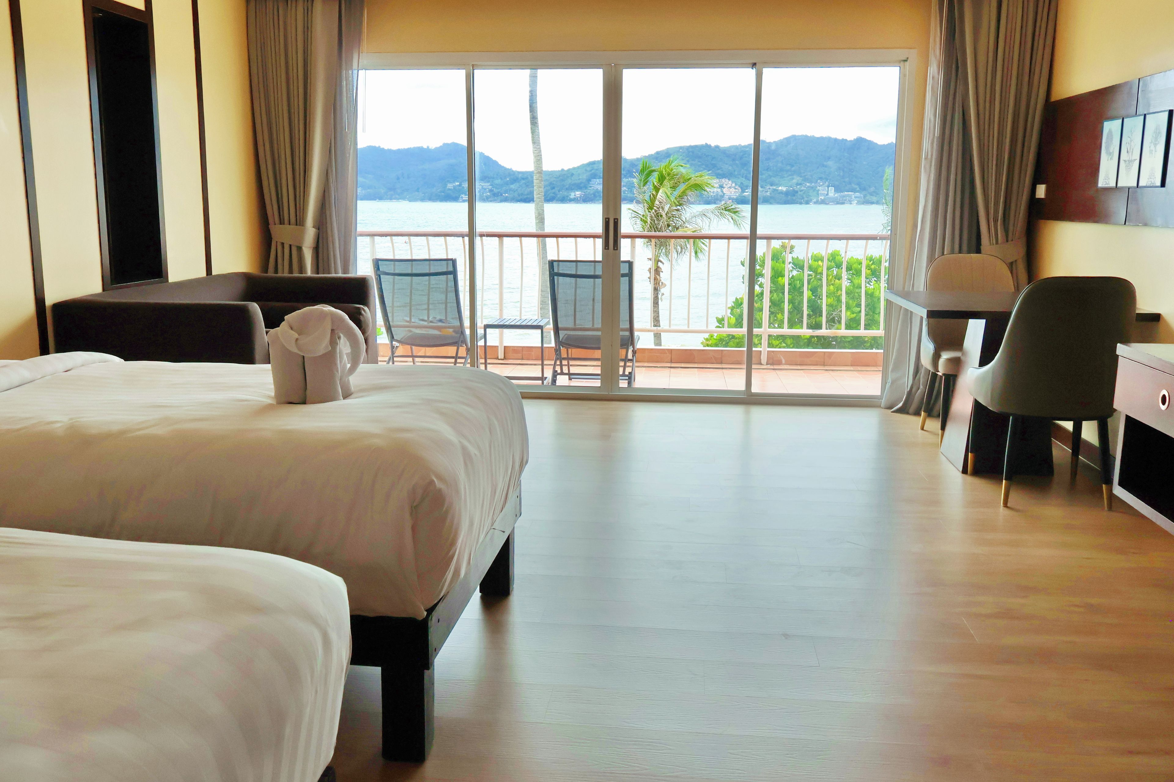 A hotel room with two beds, a desk, a chair, and a view of the sea.