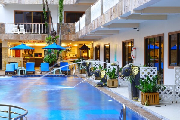 A pool area with lounge chairs, umbrellas, and decorative elephant statues.