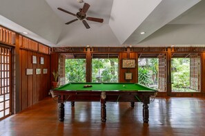 A pool table in a room with wooden paneling and large windows.