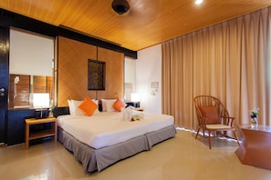 A hotel room with a large bed, a wooden headboard, a wooden nightstand, a chair, and a desk with a vase of flowers.