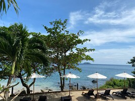A beachside lounge area with umbrellas and lounge chairs, overlooking a calm sea and a distant island.