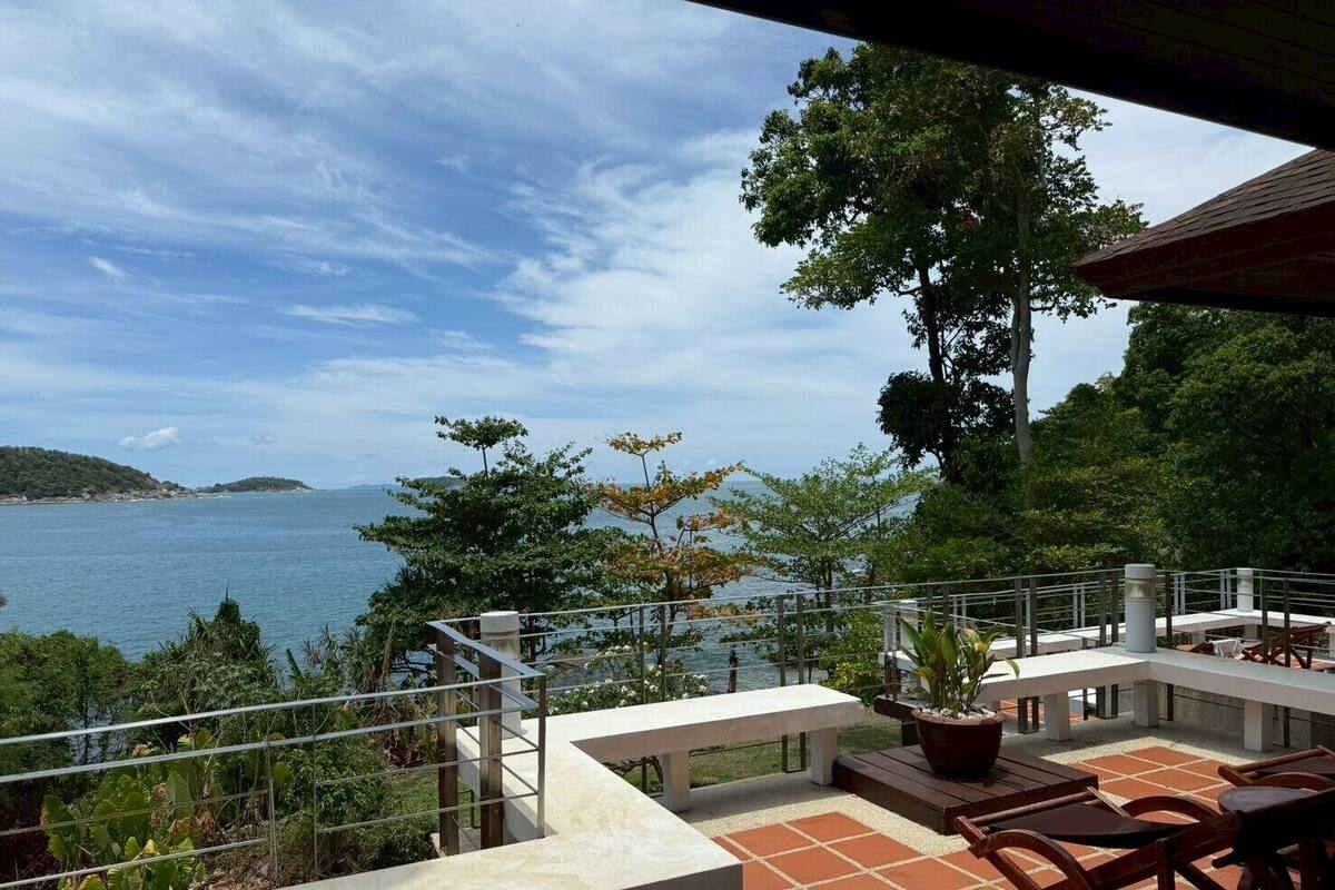 Una terraza con vista al mar, mobiliario exterior y barandilla.