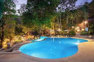 A swimming pool surrounded by trees and lounge chairs, with a building in the background.