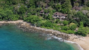 An aerial view of a coastal property with multiple houses surrounded by dense greenery and a rocky shoreline.