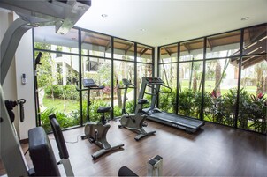 A gym with exercise equipment and large windows overlooking a garden.