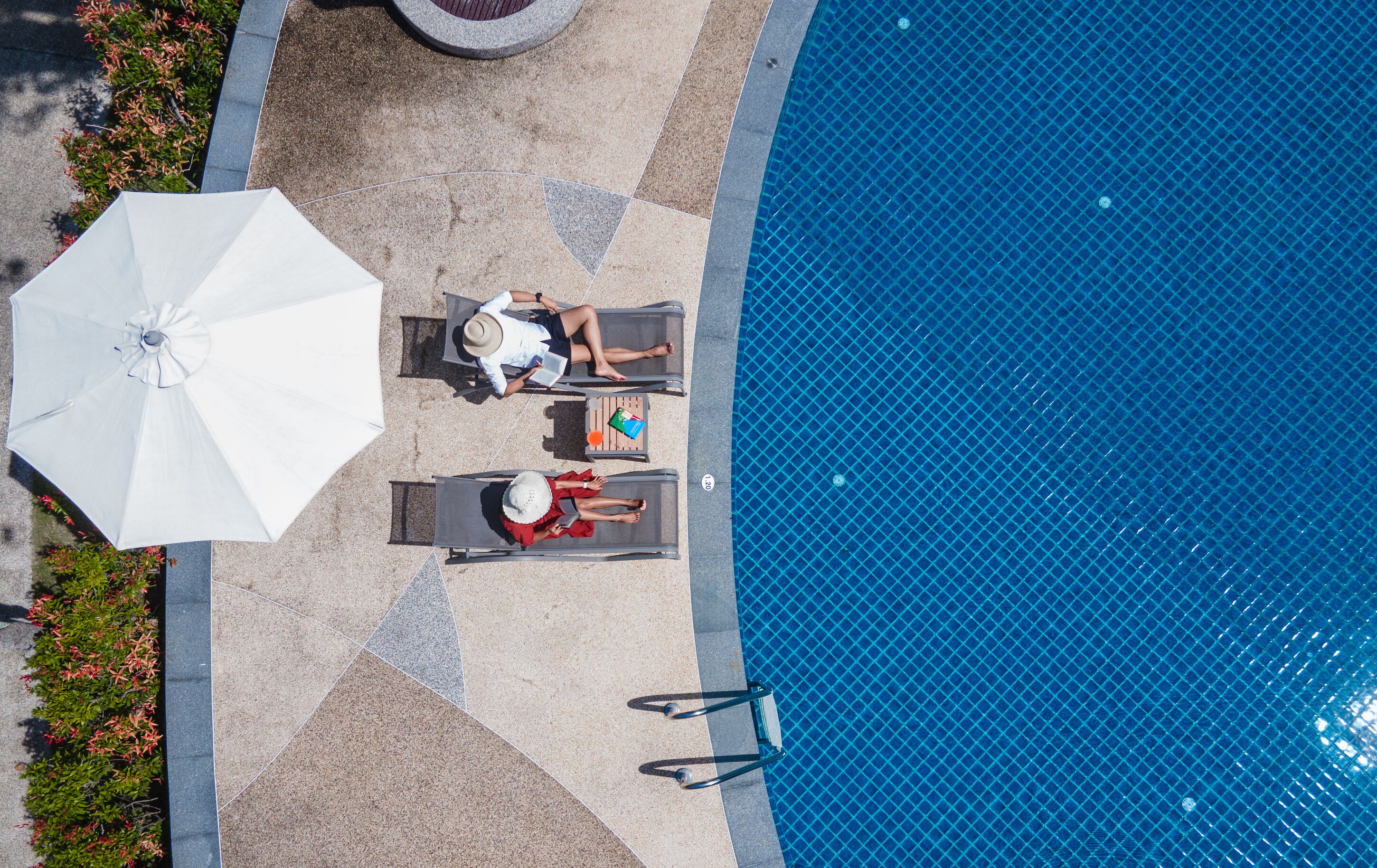 Vista aérea de una zona de piscina con sillones de descanso y una sombrilla.