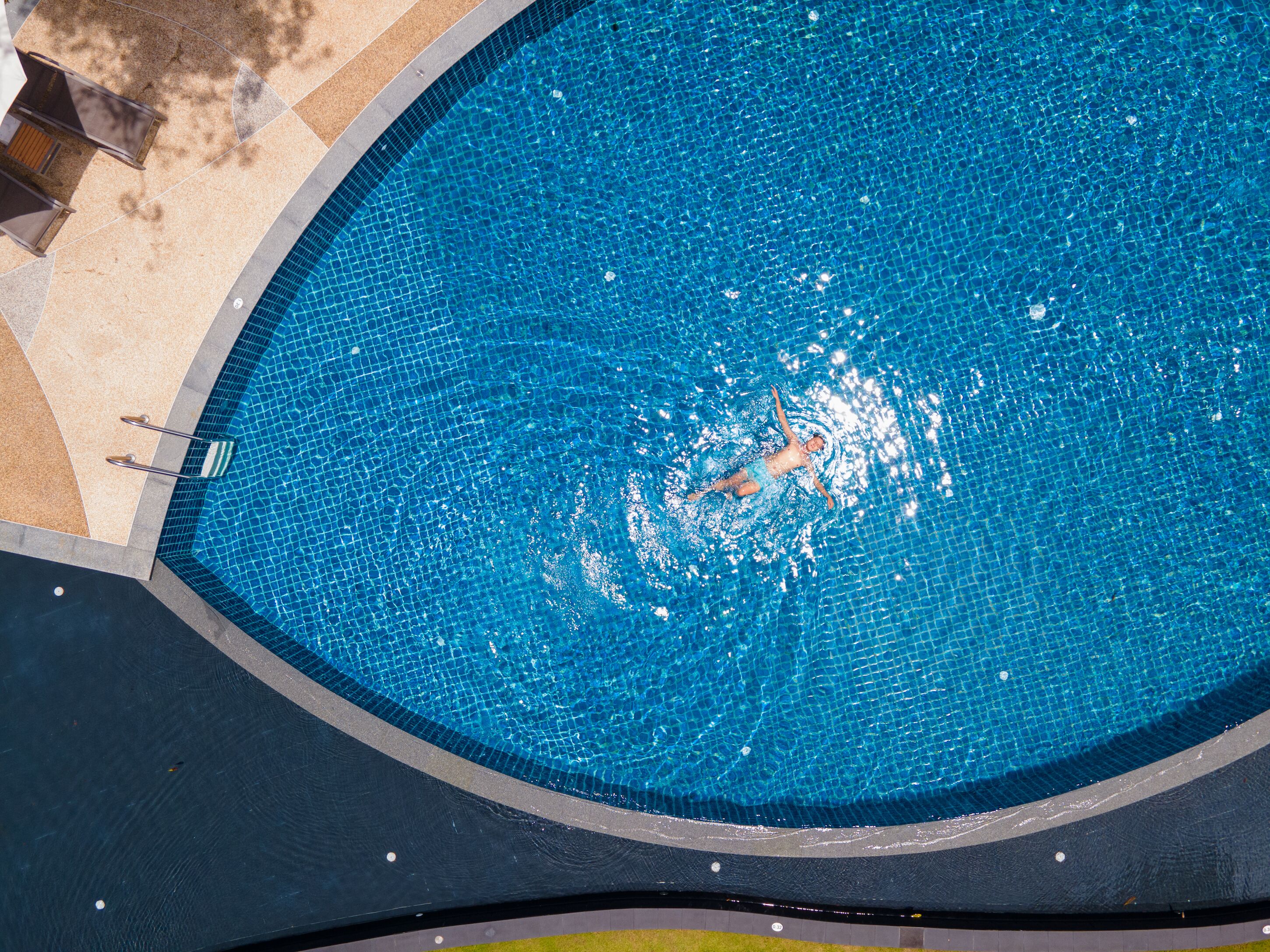 A swimming pool with a person swimming, surrounded by a tiled deck and a curved edge.