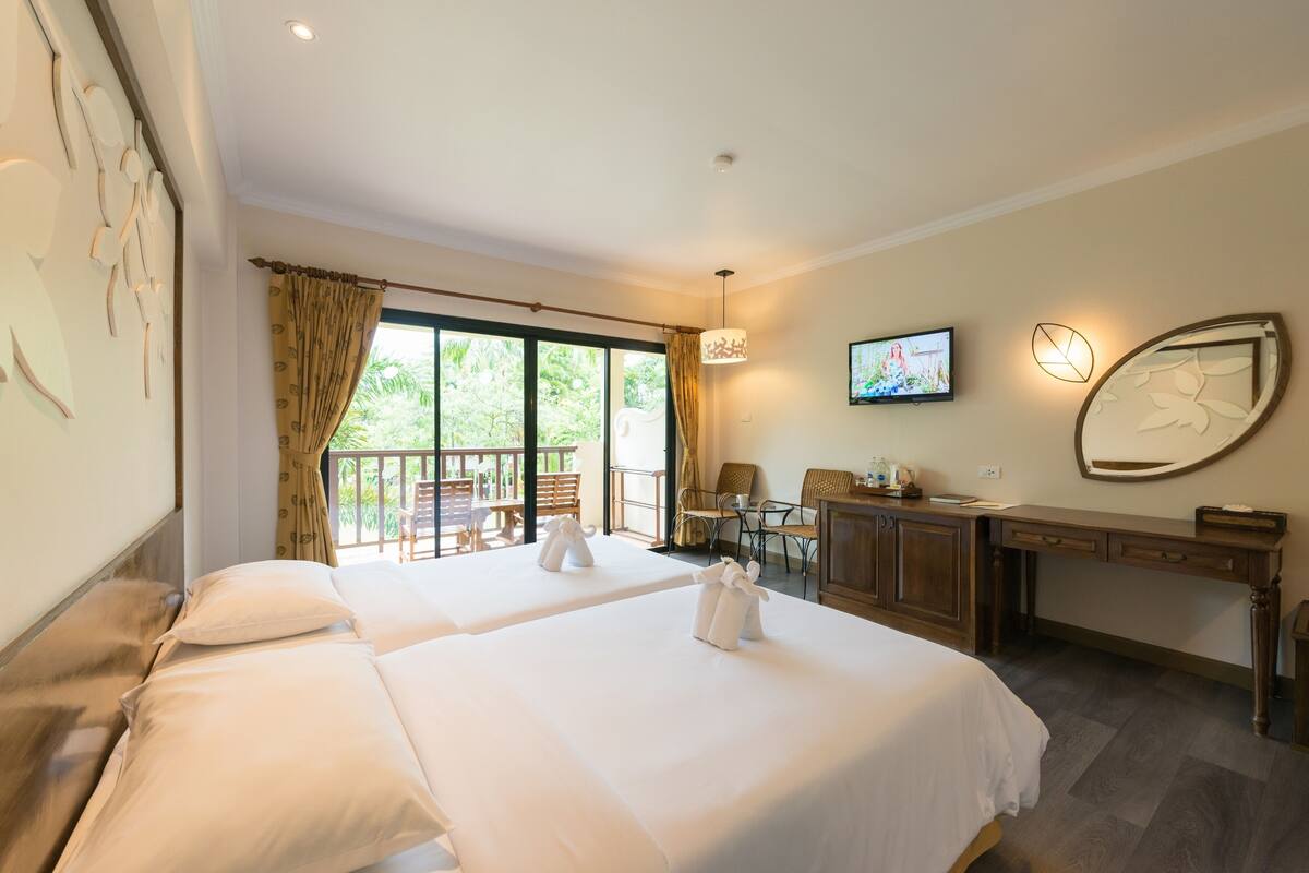 Una habitación de hotel con dos camas, un escritorio, televisión y un balcón con mobiliario exterior.