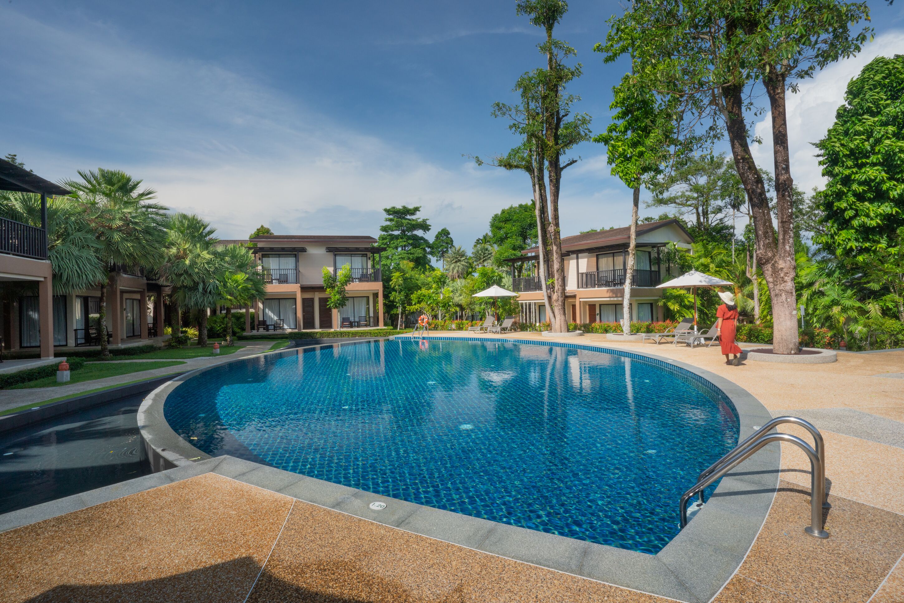 A swimming pool surrounded by buildings with balconies, palm trees, and lounge chairs.
