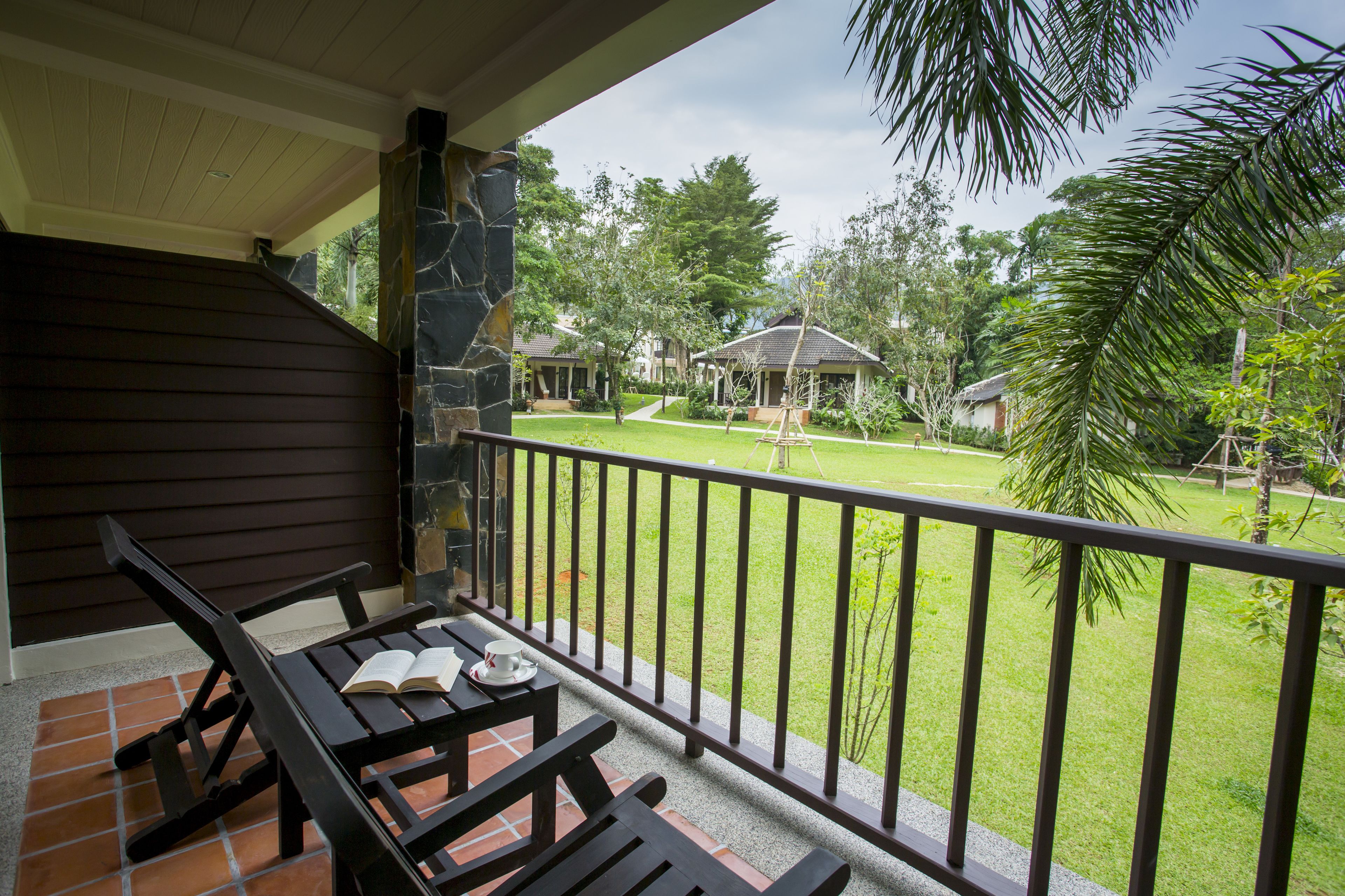 A balcony with a table and chairs, overlooking a well-maintained lawn and a building in the background.