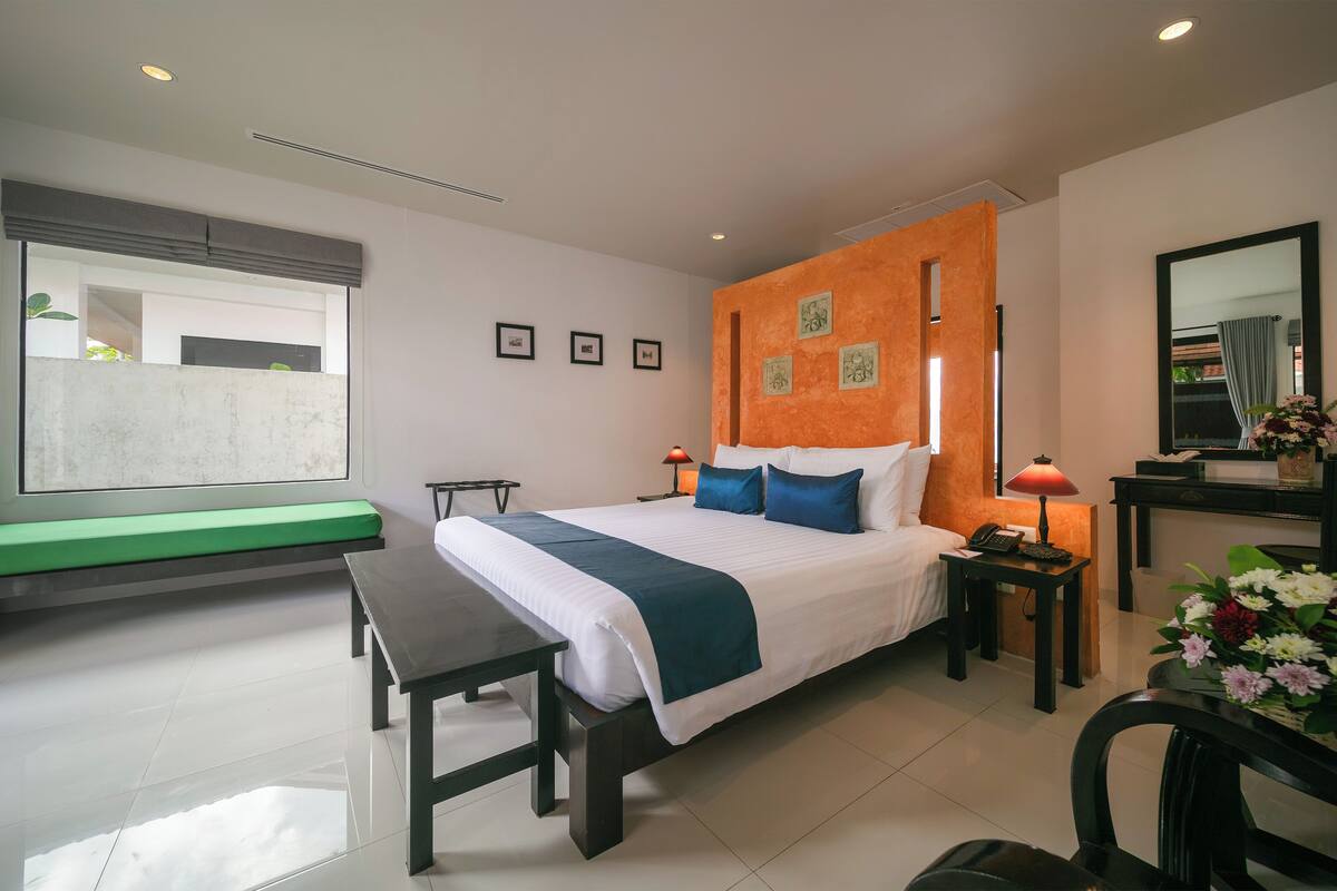 Een moderne hotelkamer met een groot bed, nachtkastjes, een bankje, een bureau en een spiegel.