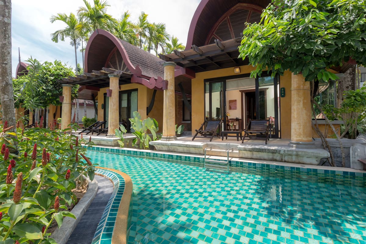 A pool area with a checkered tile pattern, surrounded by palm trees and a building with arched windows and columns.