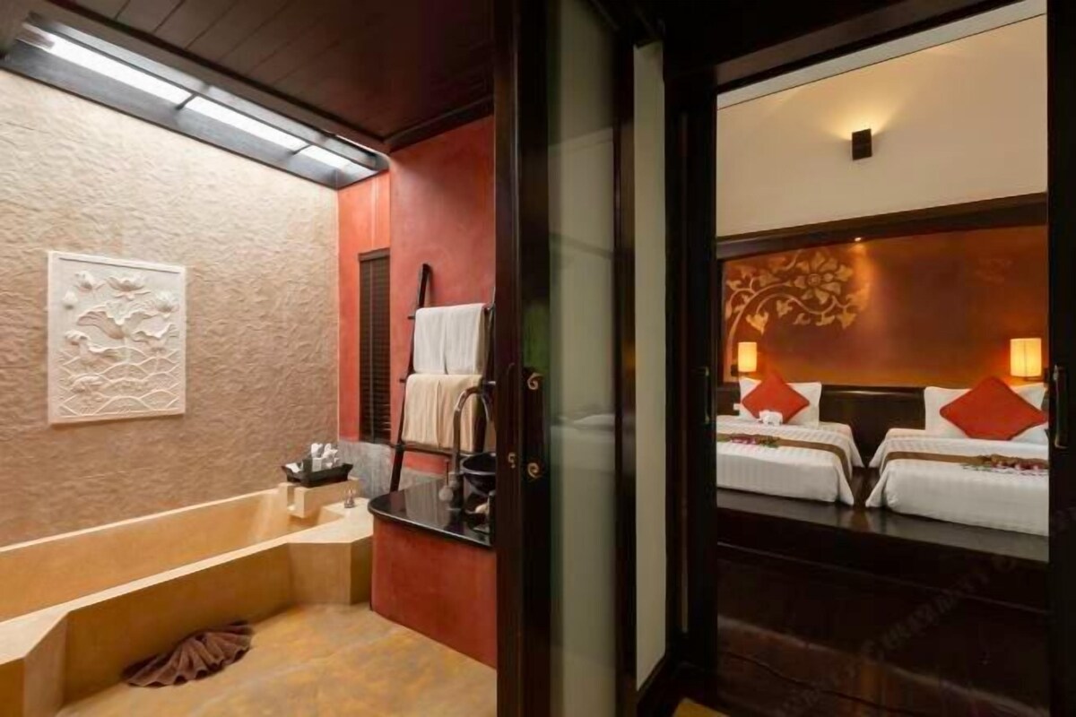 Een hotelkamer met een badkuip, een wastafel en twee bedden met rode kussens.