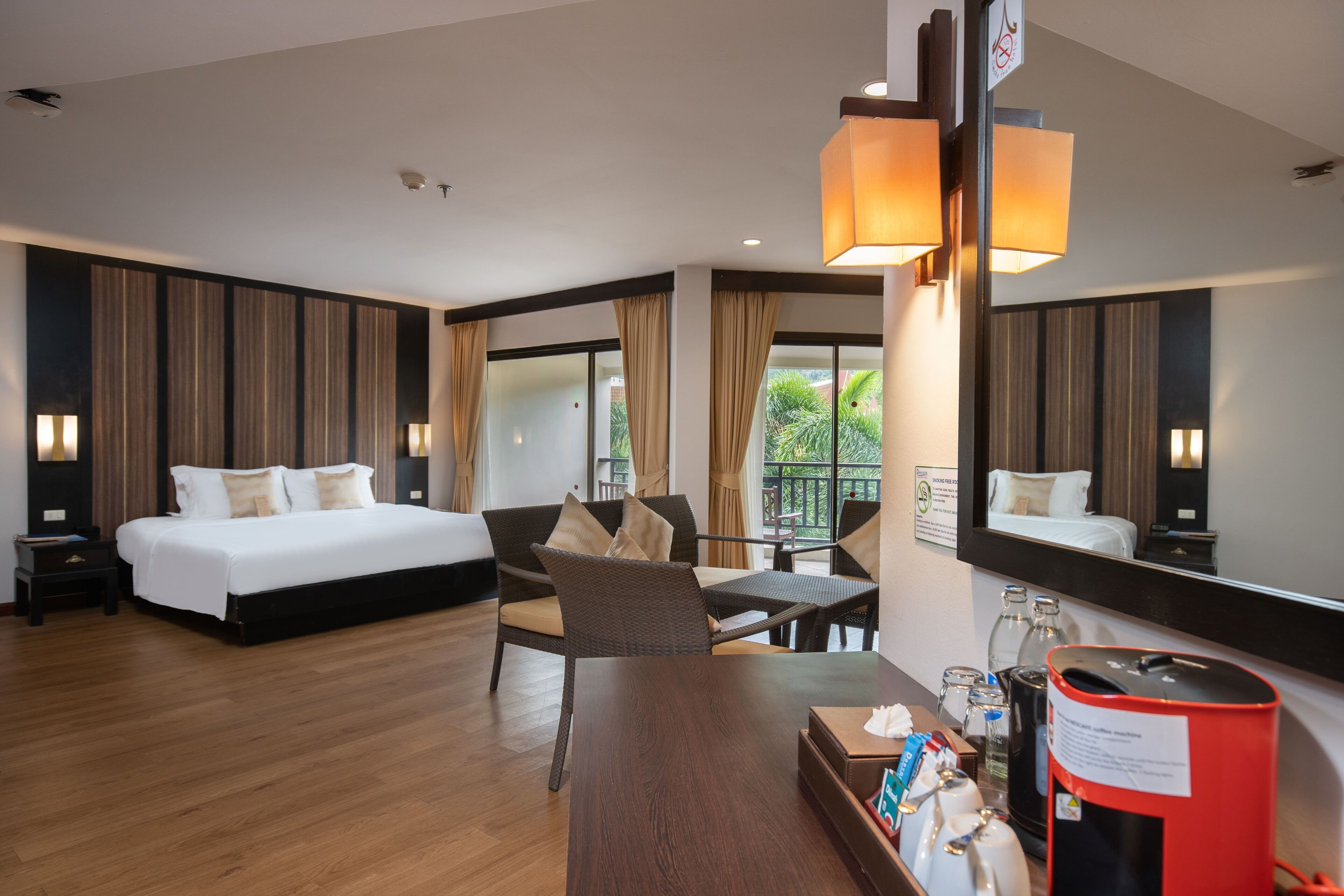 A hotel room with a bed, a dining table, a chair, a coffee machine, and a large mirror.