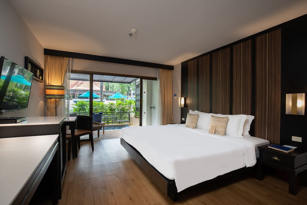 A modern hotel room with a large bed, a desk with a TV, and a balcony with umbrellas.