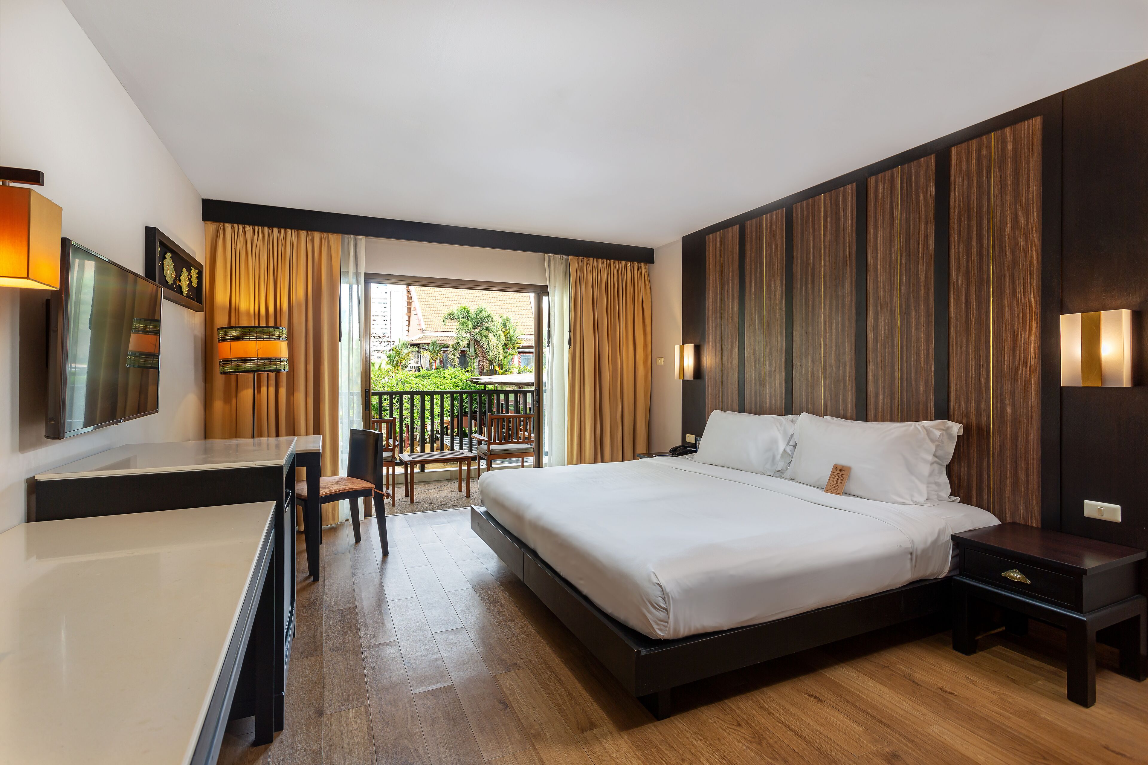A modern hotel room with a large bed, a desk, and a balcony with outdoor seating.