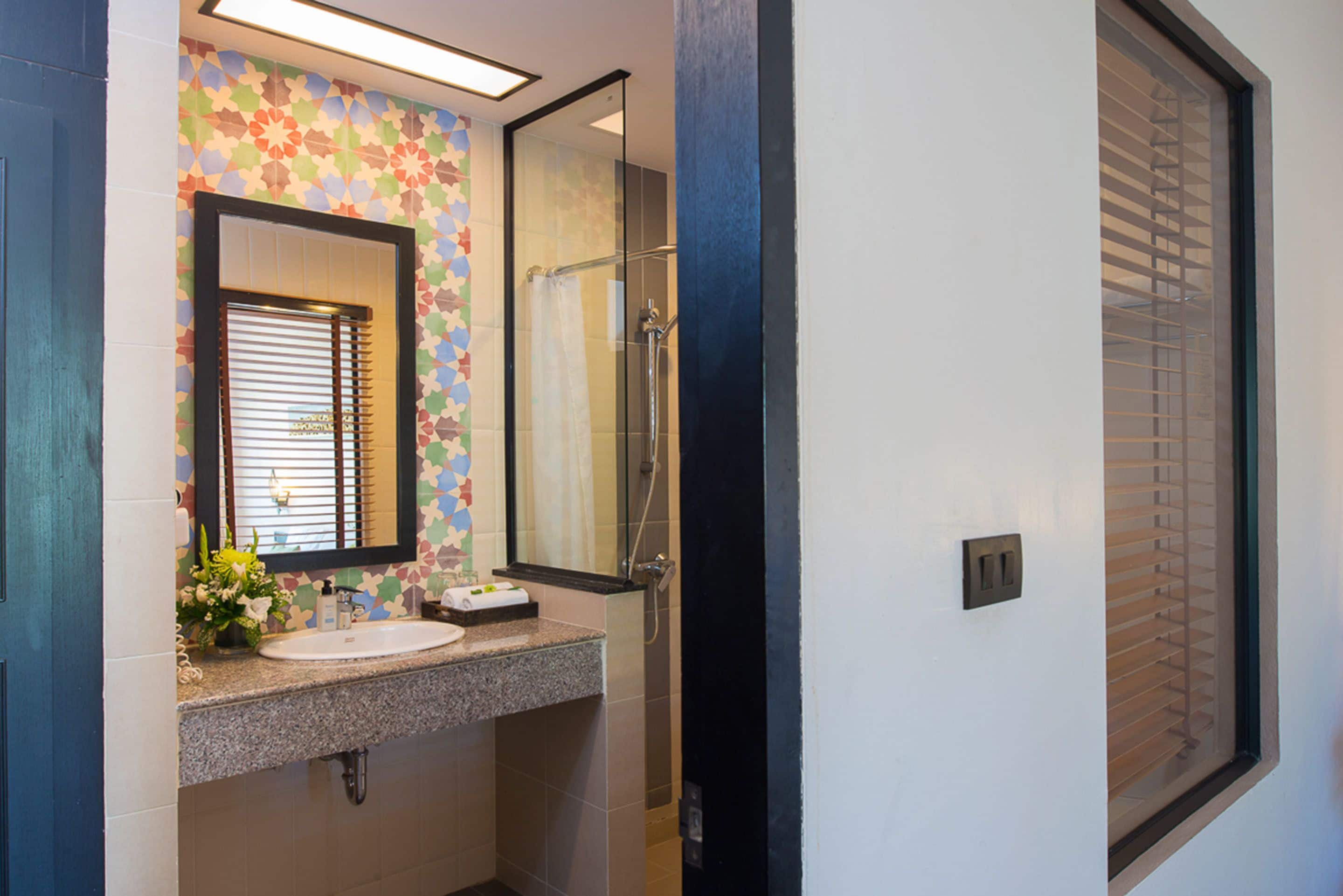 A bathroom with a sink, mirror, shower, and a window with blinds.