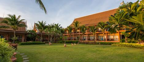 A hotel courtyard with a large building, palm trees, and a well-maintained lawn.