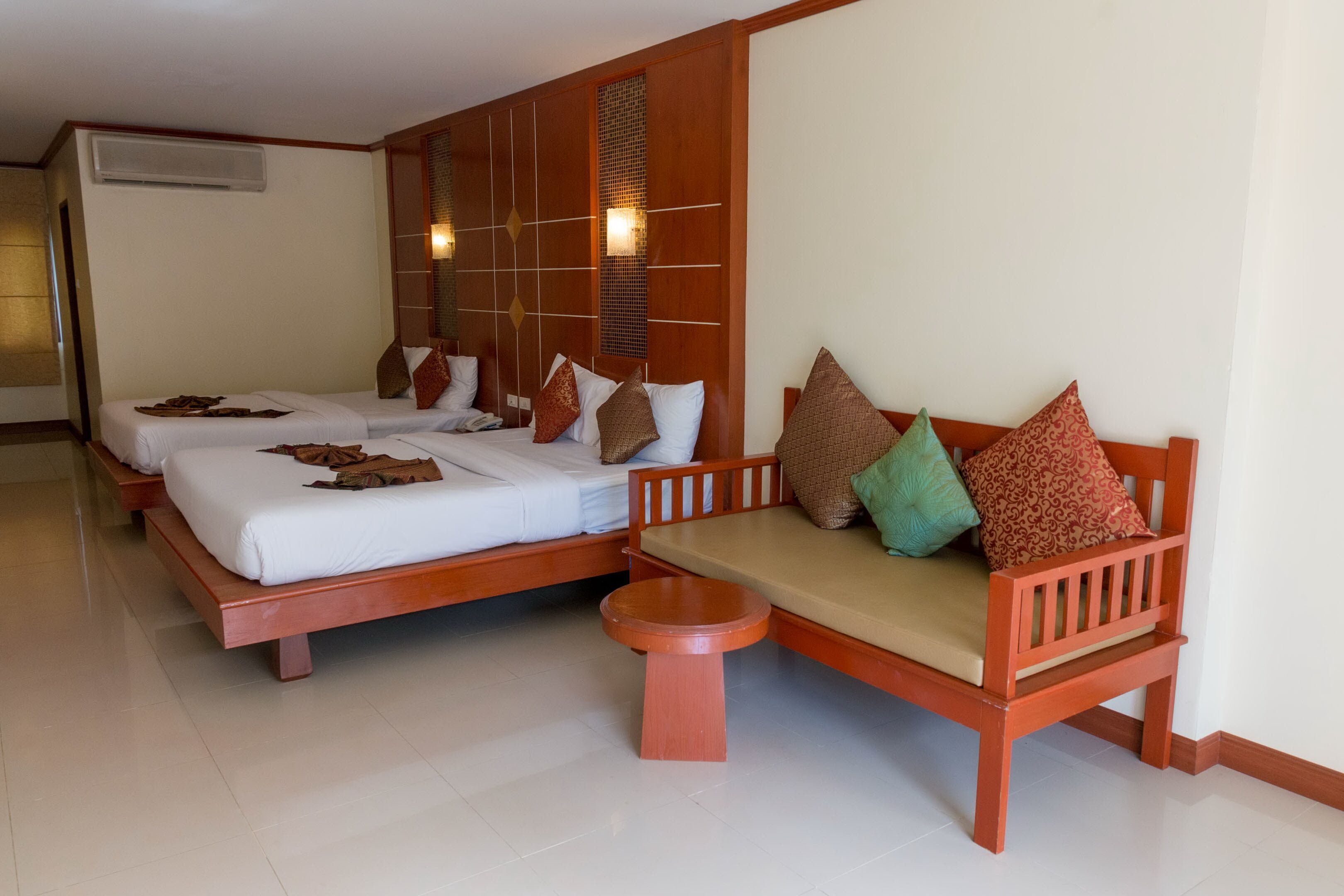 A hotel room with two wooden beds, a sofa, and a small stool.