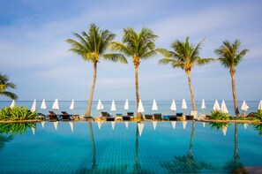 A poolside area with lounge chairs and umbrellas, palm trees, and a view of the ocean. - Lanta Casuarina Beach Resort (Ko Lanta)