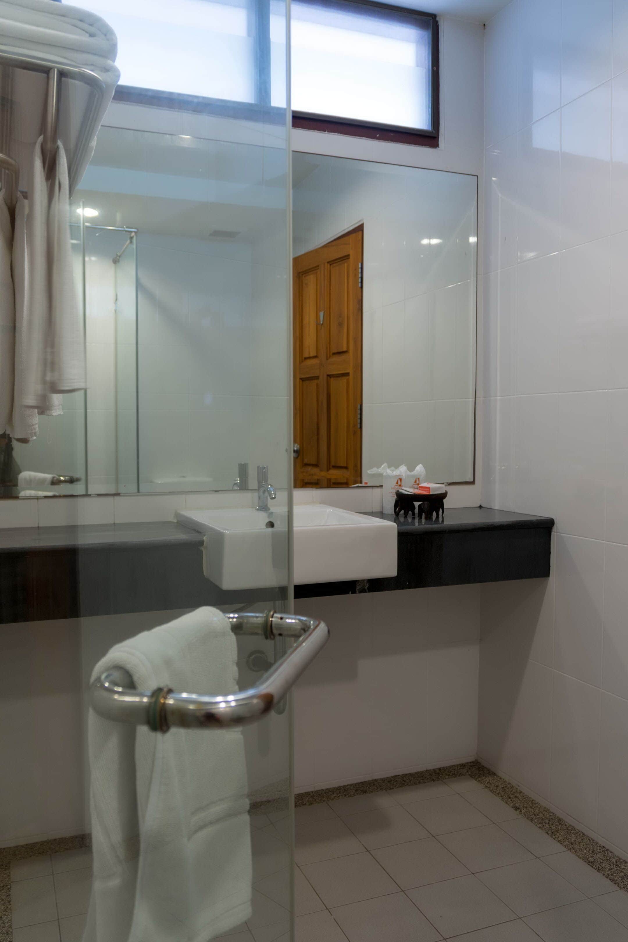 A modern bathroom with a glass shower enclosure, a white sink, and a wooden door.
