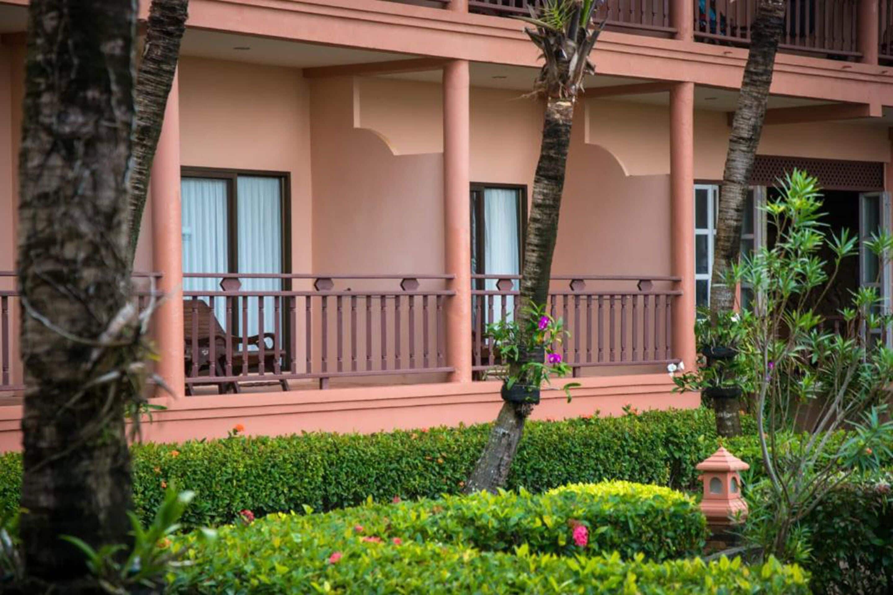 A hotel with a two-story structure, balconies with railings, and a well-maintained garden with various plants and a small decorative lamp.